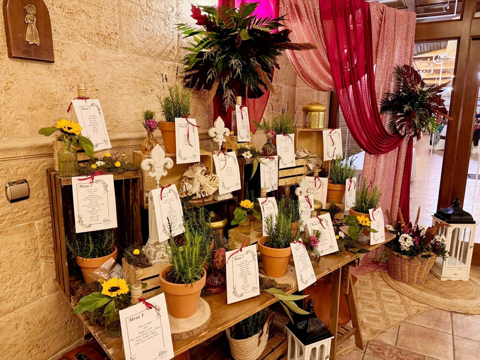 Protocolo de invitados: tarjetas de cada mesa entre macetas de romero, girasoles y cajas de madera