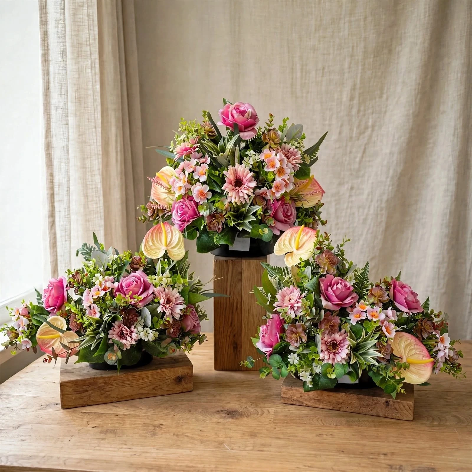 Tres centros de flor artificial en tonos rosa, con rosas, gerberas y anturios