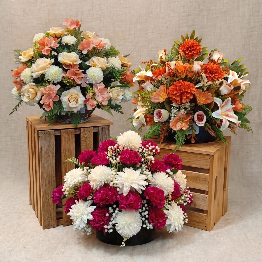 Tres centros de flor artificial: claveles fucsia y blancos, dalias naranjas y rosas color melocotón